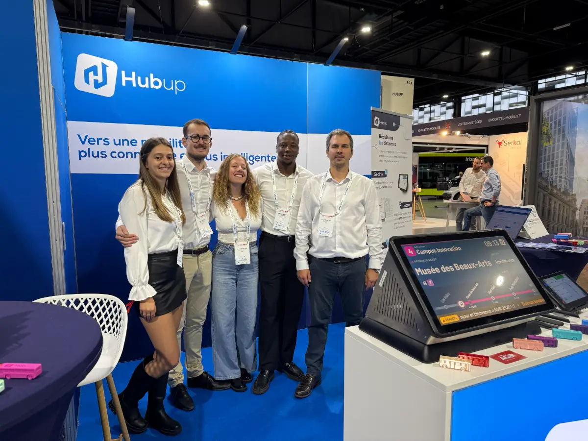 Part of the Hubup team on the Hubup stand, in front of a passenger information display