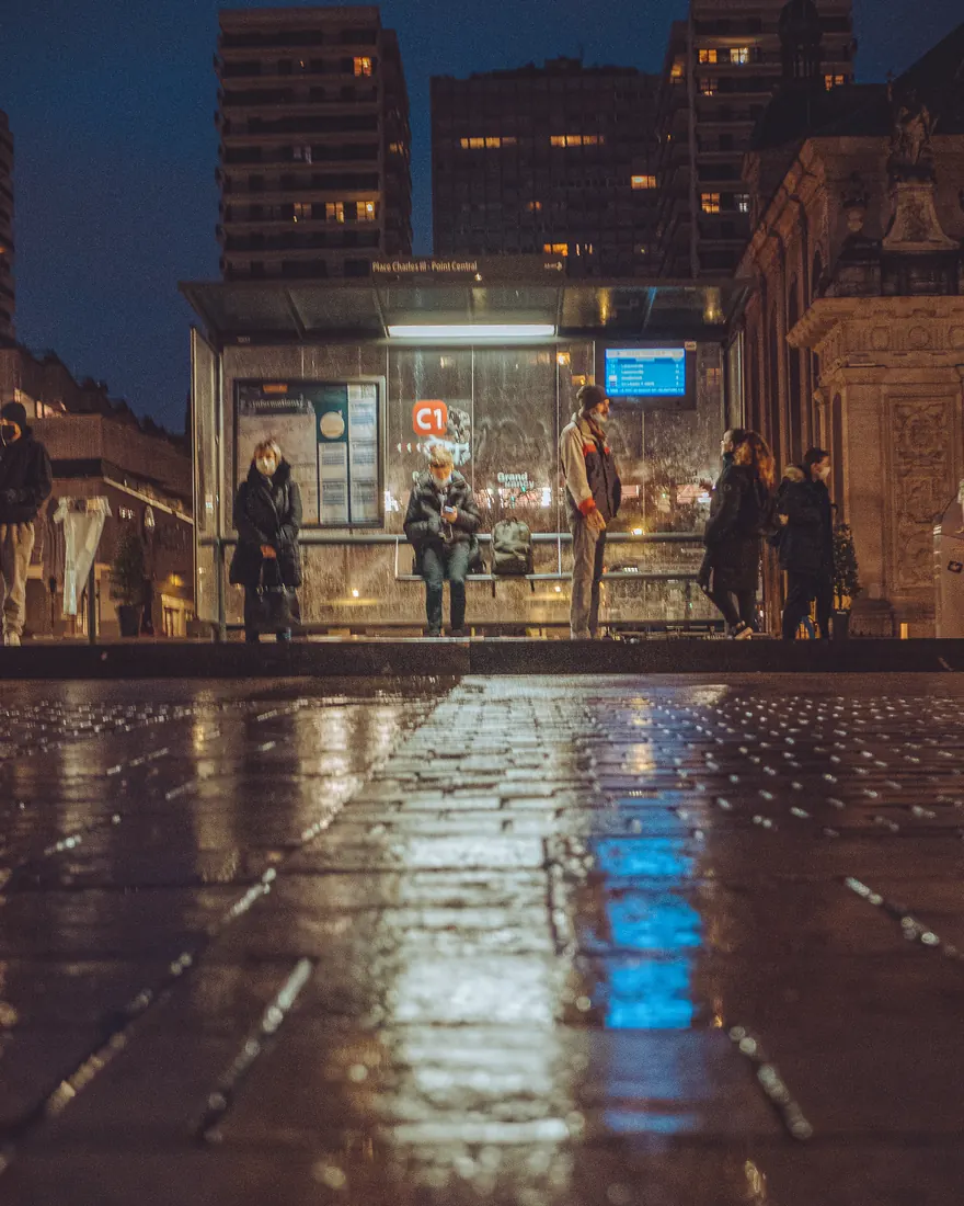 Passengers waiting for the bus at night under a shelter with a passenger information display